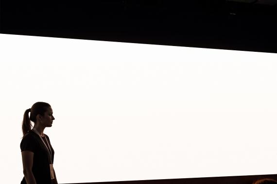 Conference Stage Presentation Screen Mockup – Empty White Display with Silhouetted Host